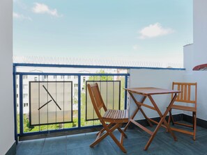 Un balcon avec une table et deux chaises, une vue sur un immeuble et une rambarde bleue.
