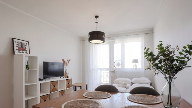A dining area with a wooden table, four chairs, a television on a white cabinet, and a vase with a plant. - Długa Homely Apartment (Toruń)