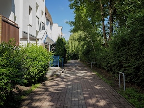 A paved pathway leading to a building with a blue gate, surrounded by greenery and trees. - Długa Homely Apartment (Toruń)