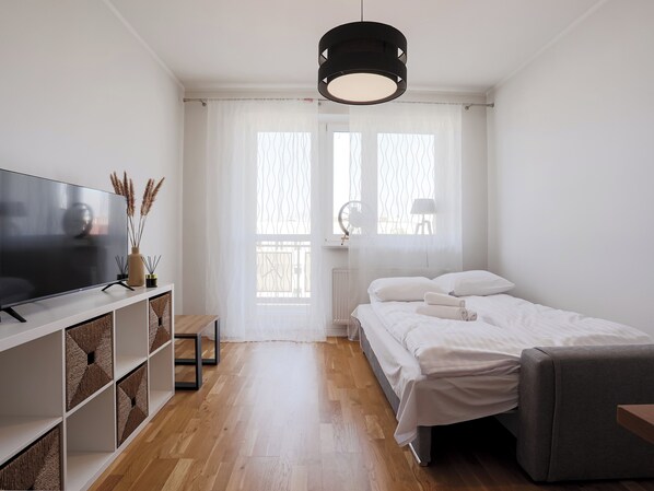 Une chambre moderne avec un lit, une télévision, une table de chevet et une fenêtre ornée de rideaux légers.