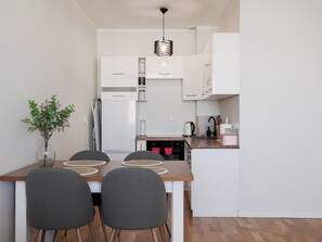 Une cuisine moderne avec des meubles blancs, une table à manger en bois et quatre chaises, ainsi qu’un luminaire suspendu.