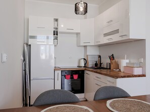 A compact kitchen with white cabinets, a built-in oven, a coffee maker, and a dining table with chairs. - Długa Homely Apartment (Toruń)