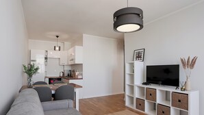 A modern living room with a sofa, a coffee table, a TV on a white console, and a kitchen in the background. - Długa Homely Apartment (Toruń)