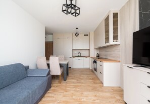 Eine moderne Küche mit weißen Schränken, ein Essbereich mit blauem Sofa und Stühlen sowie ein Fernseher auf einem weißen Schrank.