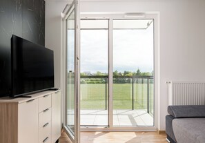 Ein modernes Zimmer mit Fernseher auf einer Holzkabine, einer Glastür zum Balkon und einem grauen Sofa.