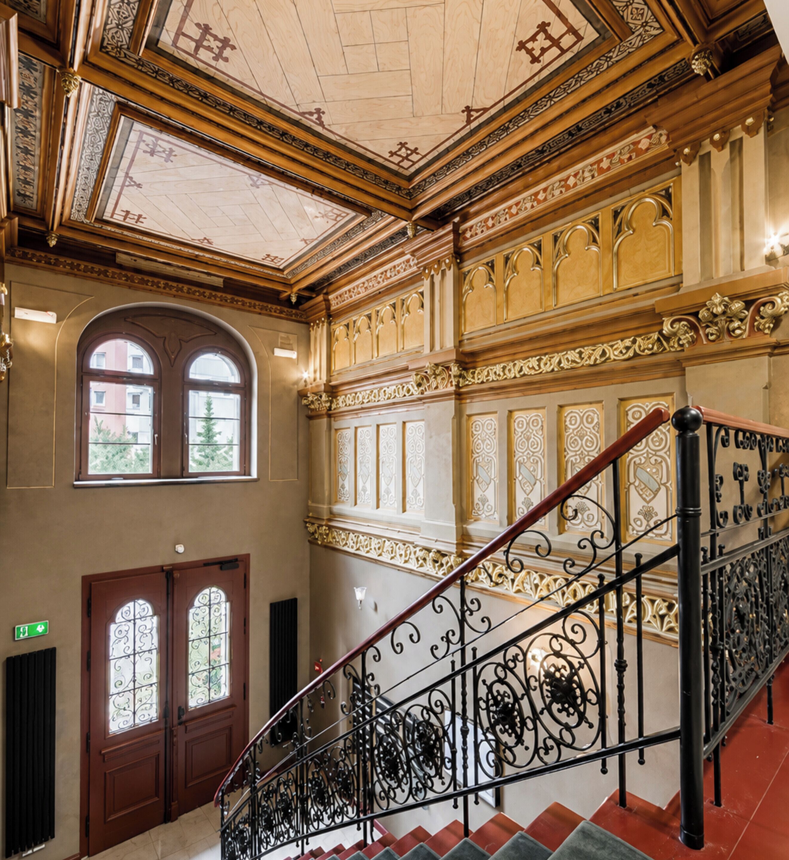 A grand staircase with ornate metal railings and a ceiling with intricate designs.