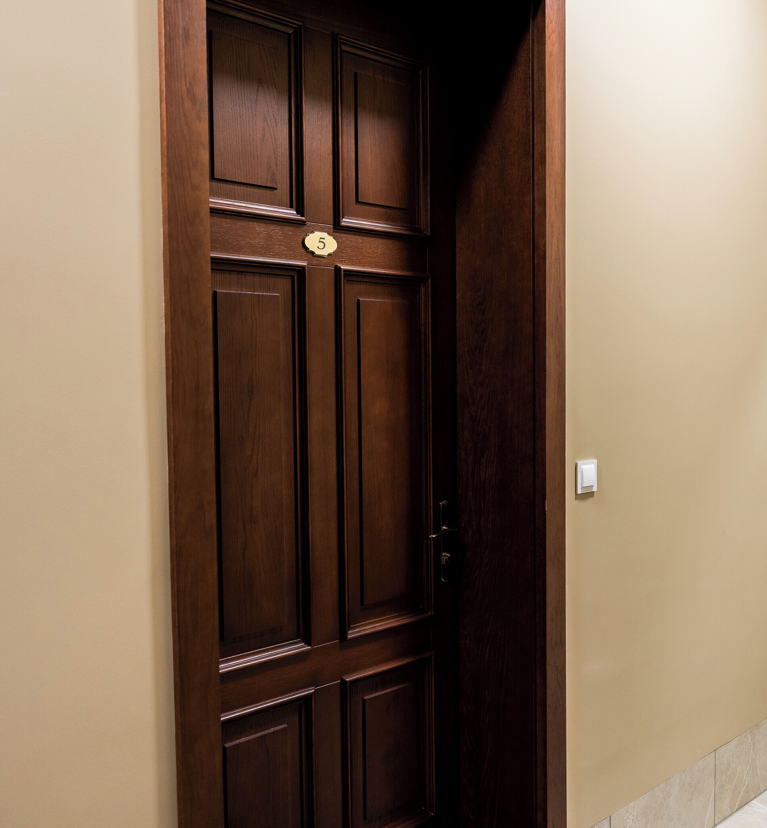 A wooden door with a number plate, a light switch, and a partial view of a beige wall.