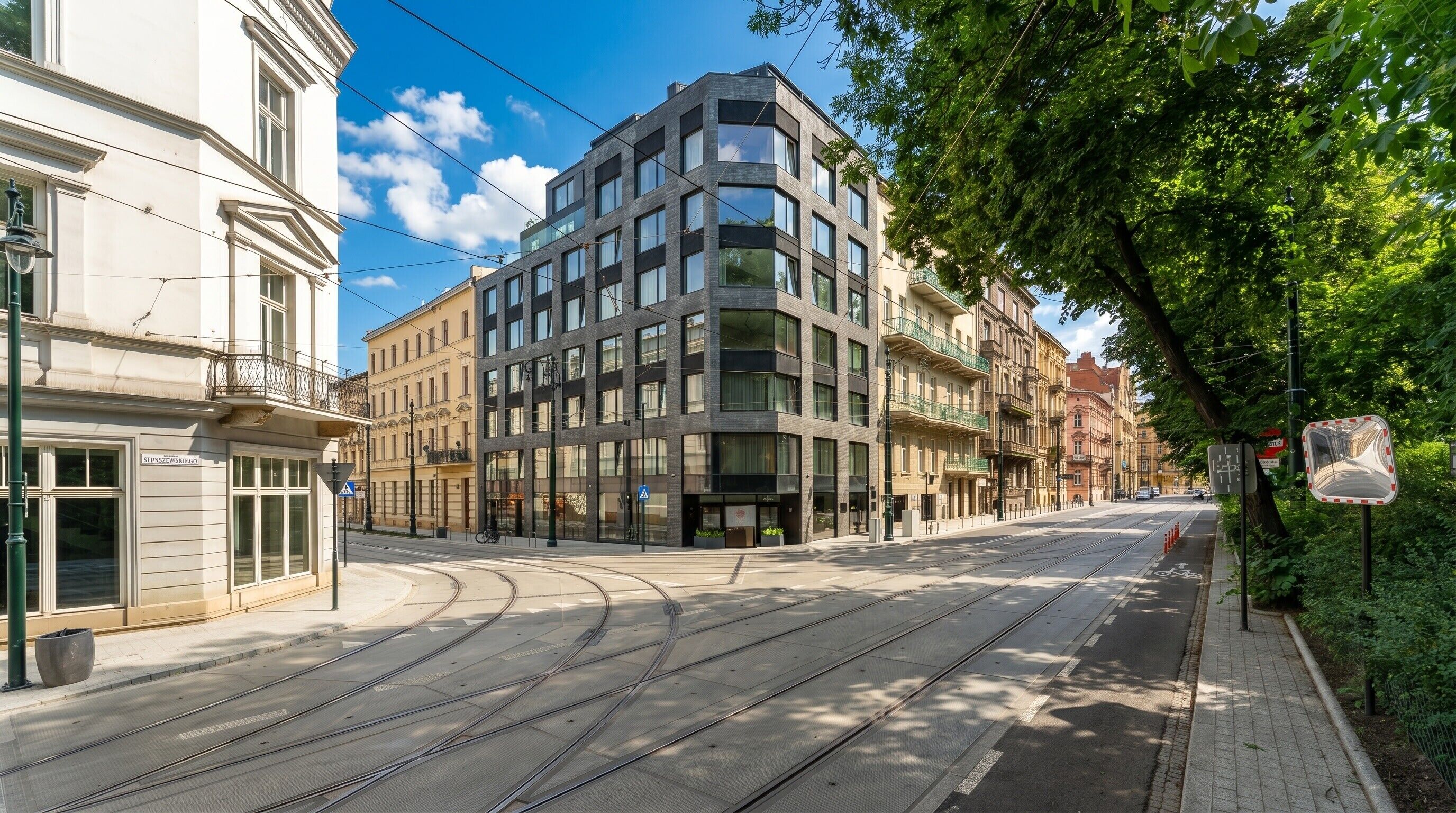 Una calle con vías de tranvía, un edificio moderno y una acera arbolada.
