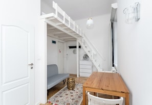 Ein gemütlicher Raum mit Holztisch, weißem Stuhl, einem gemusterten Teppich, einer blauen Couch, einer weißen Treppe und einer weißen Tür.