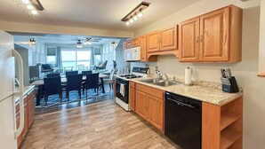 A kitchen with wooden cabinets, a dishwasher, and a dining area with chairs and a table. - Lower Lake Retreat | Charming Waterfront Stay (Seneca Falls)