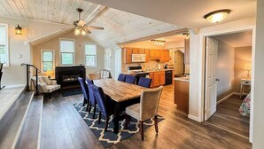 A spacious living area with a dining table, sofas, and a fireplace. There is a kitchen in the background with wooden cabinets and a microwave. - Lower Lake Retreat | Charming Waterfront Stay (Seneca Falls)