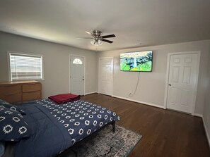 A bedroom with a bed, a ceiling fan, a TV mounted on the wall, and a window with blinds. - Charming house in lovely Birmingham with cool AC for relaxing stays (Birmingham)