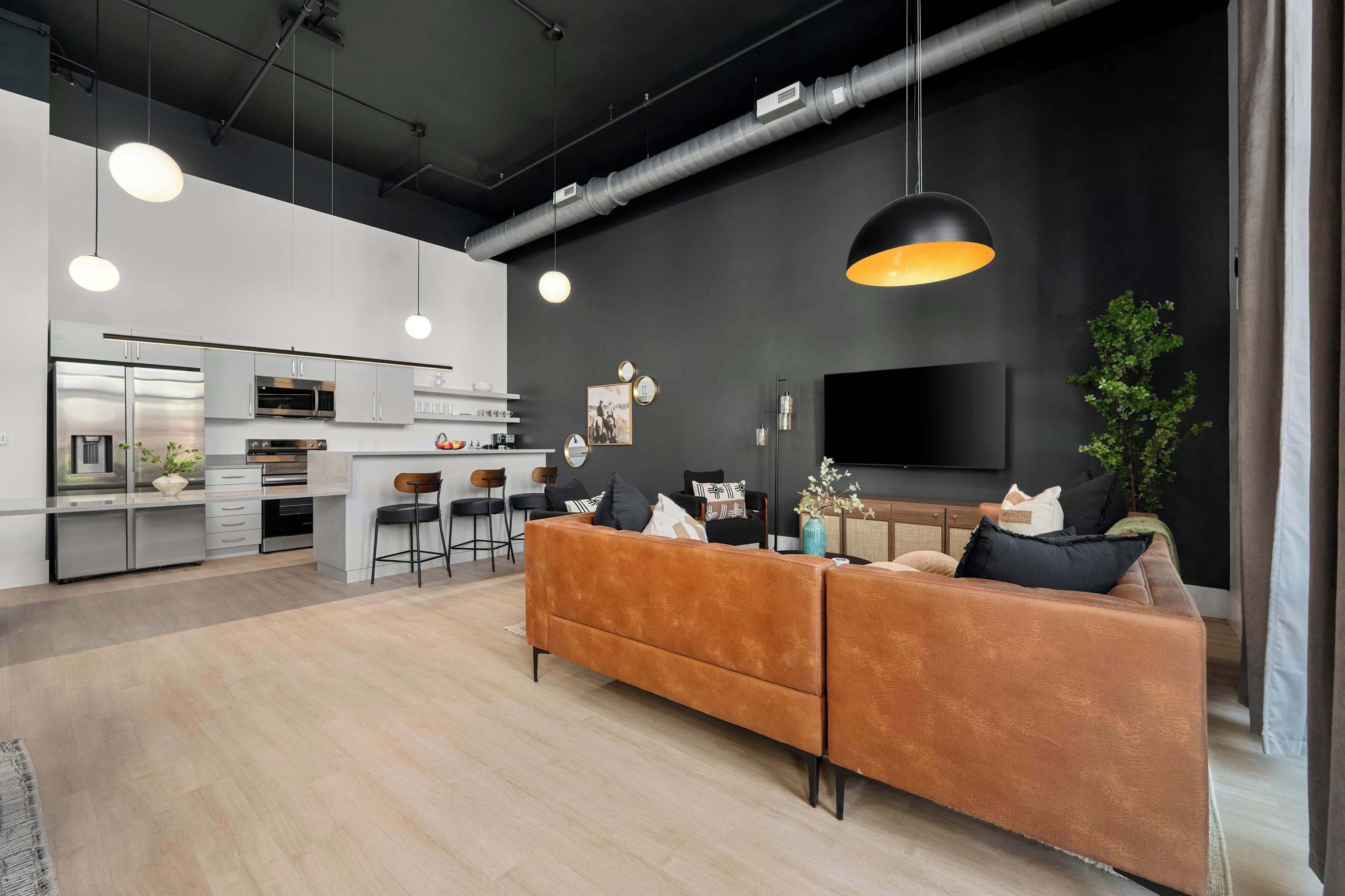 A modern living space with a sofa, dining area, kitchen, and a flat-screen TV.