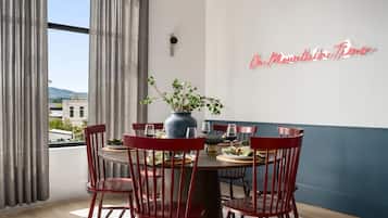 Un coin repas avec une table ronde, des chaises rouges, un vase avec des plantes vertes et un panneau lumineux au néon sur le mur.