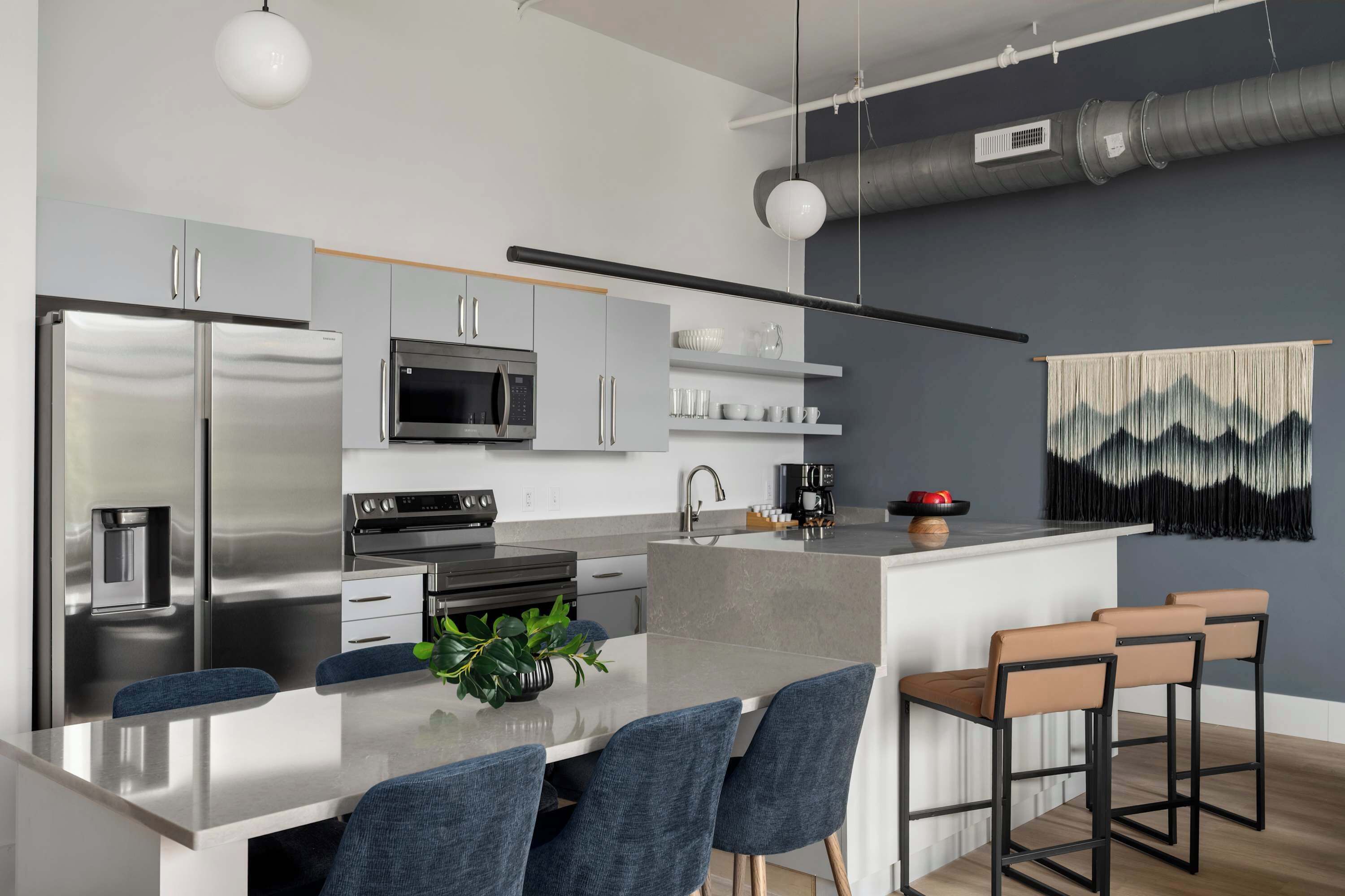 Een moderne keuken met roestvrijstalen apparatuur, een centraal eiland met barstoelen en een hangende lamp.