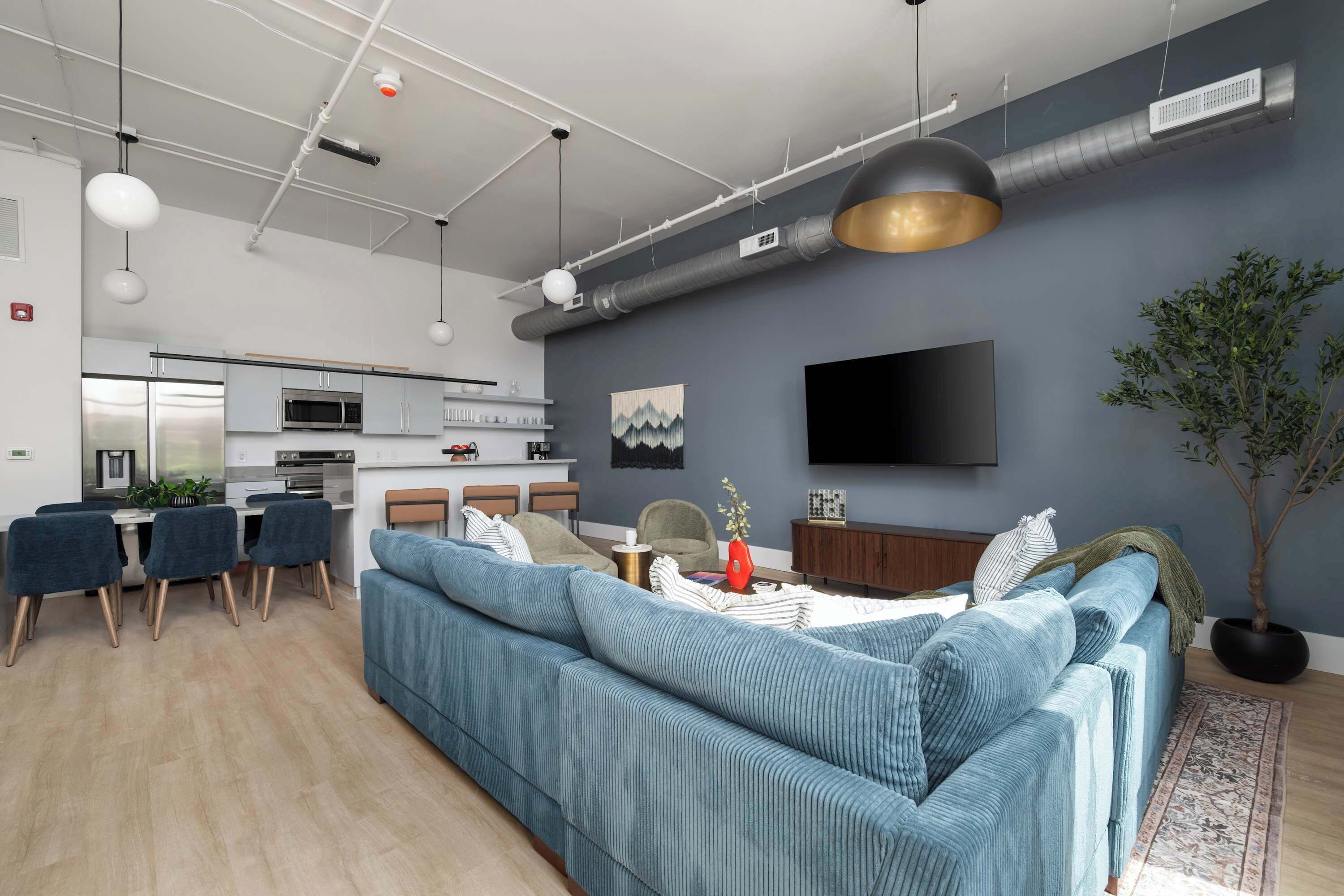 Een moderne woonkamer met een bank, eethoek, keuken en een flatscreen televisie aan de muur.