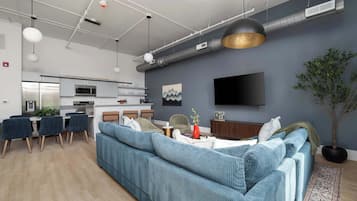 Een moderne woonkamer met een bank, eethoek, keuken en een flatscreen televisie aan de muur.