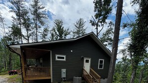 En stuga med en veranda, en liten terrass och en eldstad på gården.