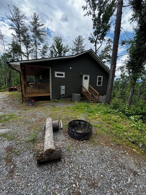 Une cabane avec un porche, une petite terrasse et un foyer extérieur dans le jardin.