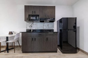 Eine moderne Küche mit dunklen Holzschränken, einer schwarzen Mikrowelle, einem Einbauofen, einem schwarzen Kühlschrank und einer Marmor-Spritzschutzwand.