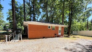 A small brick building with a covered porch, a gravel driveway, and tall trees in the background. - Parthenia's Love Shack (Durham)