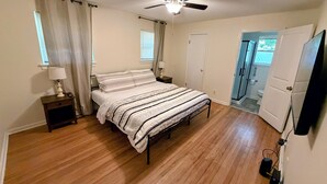 A bedroom with a bed, bedside tables, a ceiling fan, and a door leading to a bathroom. - Parthenia's Love Shack (Durham)