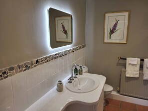 Ein Badezimmer mit einem weißen Waschbecken, einem Spiegel, einer Toilette und zwei gerahmten Blumenbildern an der Wand.