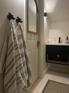 Un baño con toallero, espejo, lavabo con artículos de aseo y alfombra verde.