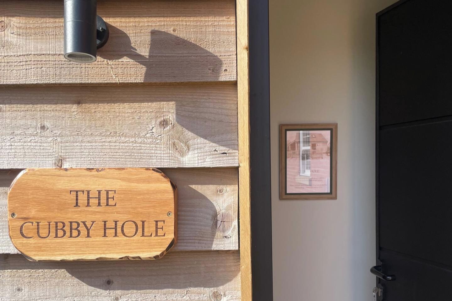 A wooden sign with 'THE CUBBY HOLE' text, a framed picture on the wall, and a door.