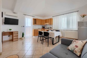 A modern kitchen with wooden cabinets, a dining table with chairs, a grey sofa, and a flat-screen TV mounted on the wall. - Holiday Apartment with Sea View (Vodnjan)
