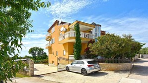 Um edifício residencial com vários andares, uma varanda, um carro estacionado e uma entrada com portão.