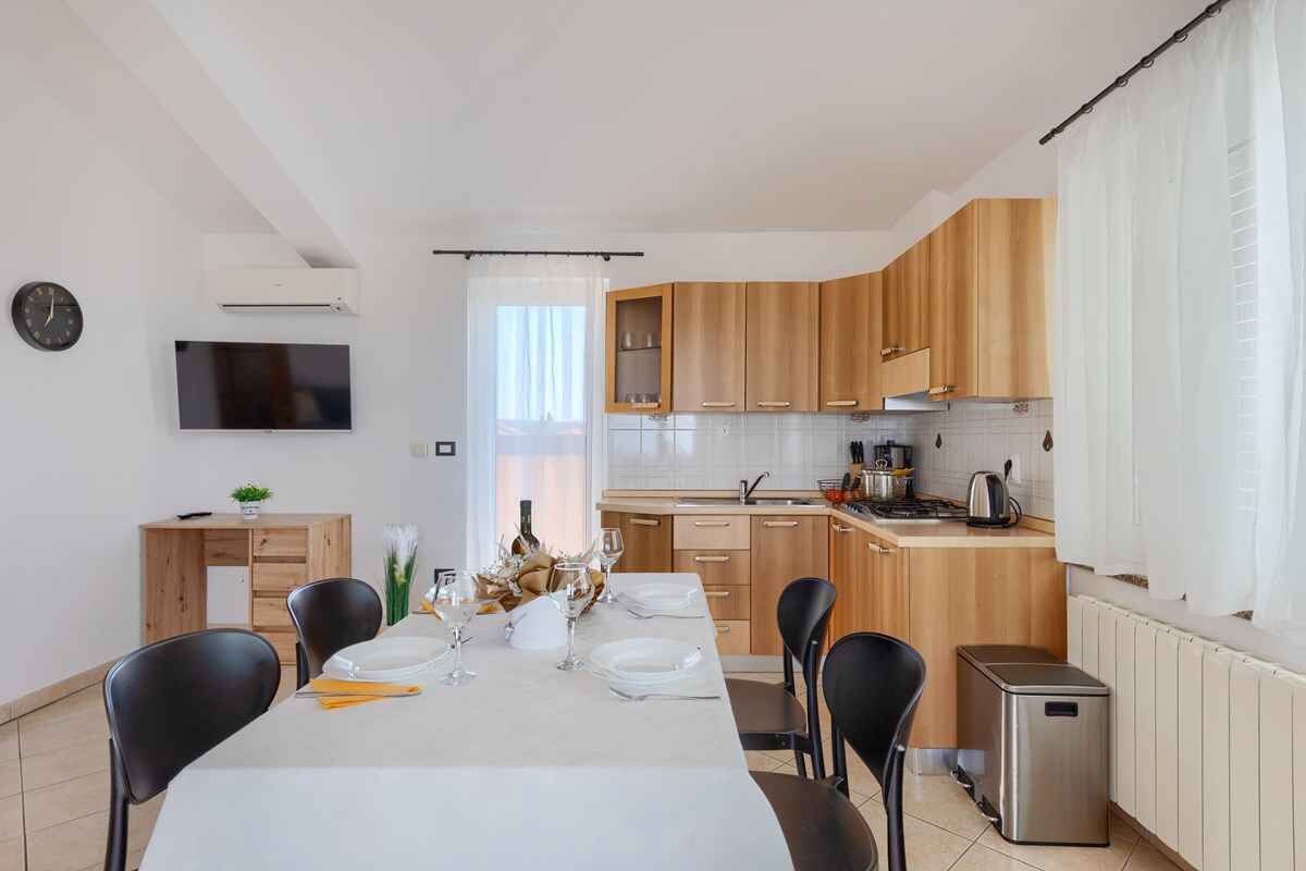 A modern kitchen with wooden cabinets, a dining table set for four, and a small trash bin.