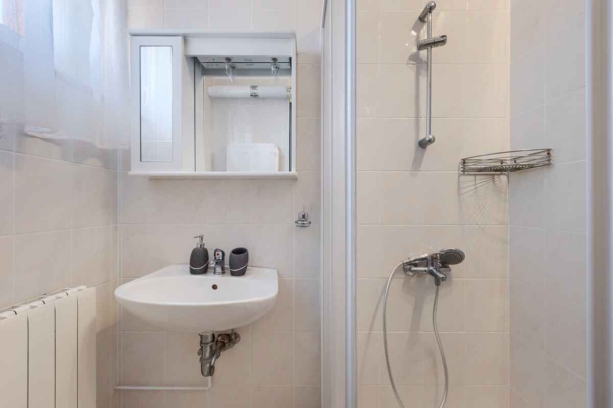A bathroom with a white sink, a mirror, a shower, and a towel rack.