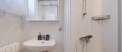 A bathroom with a white sink, a mirror, a shower, and a towel rack.