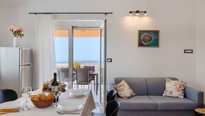 Uma área de refeições com uma mesa posta para dois, um sofá e vista através de uma porta de vidro.