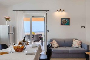 A dining area with a table set for two, a sofa, and a view through a glass door. - Holiday Apartment with Sea View (Vodnjan)