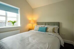 Un dormitorio con cama, mesita de noche, lámpara y ventana con vistas.