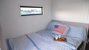 En säng med ett mönstrat överkast, en kudde med ett amerikanskt flaggmönster, ett brickbord med en kopp och ett bakverk, och ett fönster med utsikt över en byggnad.