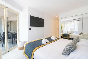 Ein modernes Hotelzimmer mit Bett, Flachbildfernseher, Essbereich und einer Schiebeglastür zum Balkon.