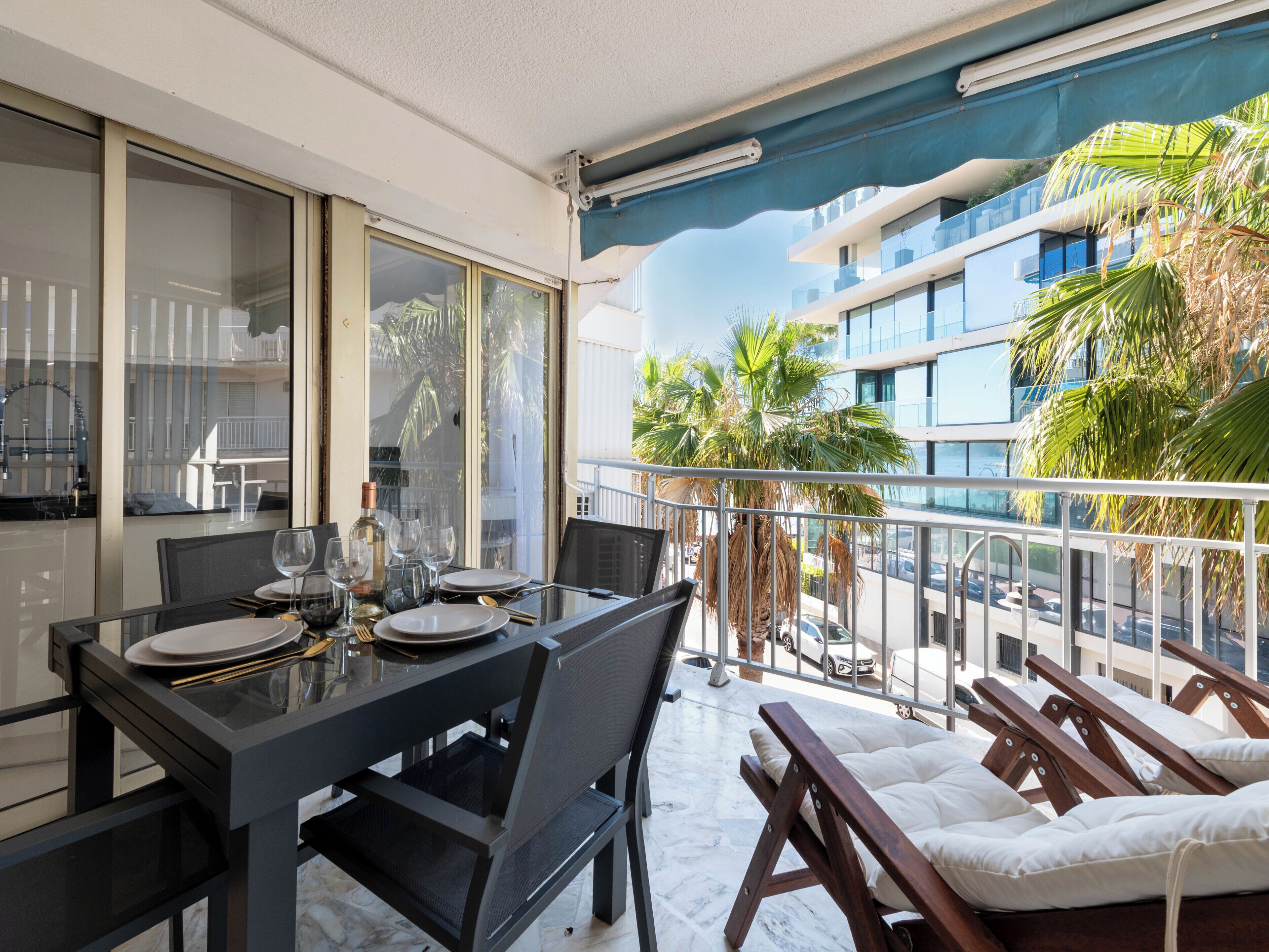A balcony with a dining table set for four, a chair, and a lounge area with cushions.