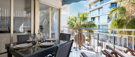 A balcony with a dining table set for four, a chair, and a lounge area with cushions.