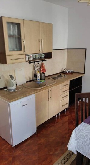 Een compacte keuken met houten kastjes, een kleine koelkast en een eethoek met een tafel en stoelen.