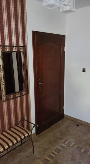 Een kamer met een houten deur, een bankje, een spiegel en vloertegels met een patroon.