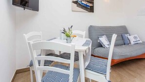 Ein Zimmer mit Esstisch, Stühlen, einer Couch, einem an der Wand befestigten Fernseher und zwei gerahmten Bildern.