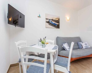 Ein Zimmer mit Esstisch, Stühlen, einer Couch, einem an der Wand befestigten Fernseher und zwei gerahmten Bildern.