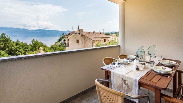 Ein Balkon mit Esstisch, der einen schönen Ausblick auf Gebäude und Berge bietet.