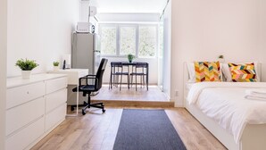 A bedroom with a bed, a desk, two chairs, a radiator, and a window. - Deda Studio w. Smart TV · AC · washing machine (Bucharest)