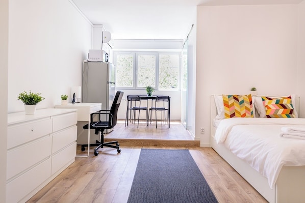 Une chambre à coucher comprenant un lit, un bureau, deux chaises, un radiateur et une fenêtre.