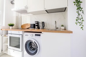 Une cuisine compacte équipée d’un lave-linge intégré, d’une machine à café et d’une petite plante en pot.