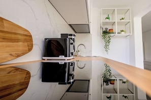 A kitchen with a modern design, featuring a black appliance, a wooden countertop, and white shelving with plants. - Deda Studio w. Smart TV · AC · washing machine (Bucharest)